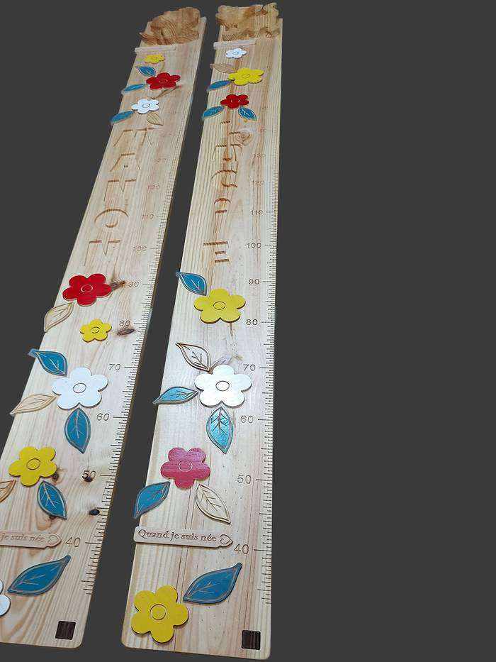 Toise personnalisée en bois pour deux soeurs, décorée de fleurs sculptées. Dans le haut, des figurines de chat et de chien.