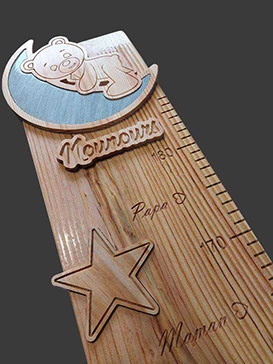 Pour cette toise en bois, le thème est le ciel étoilé. Un ourson sculpté sur son croissant de lune, avec le mot Nounours.