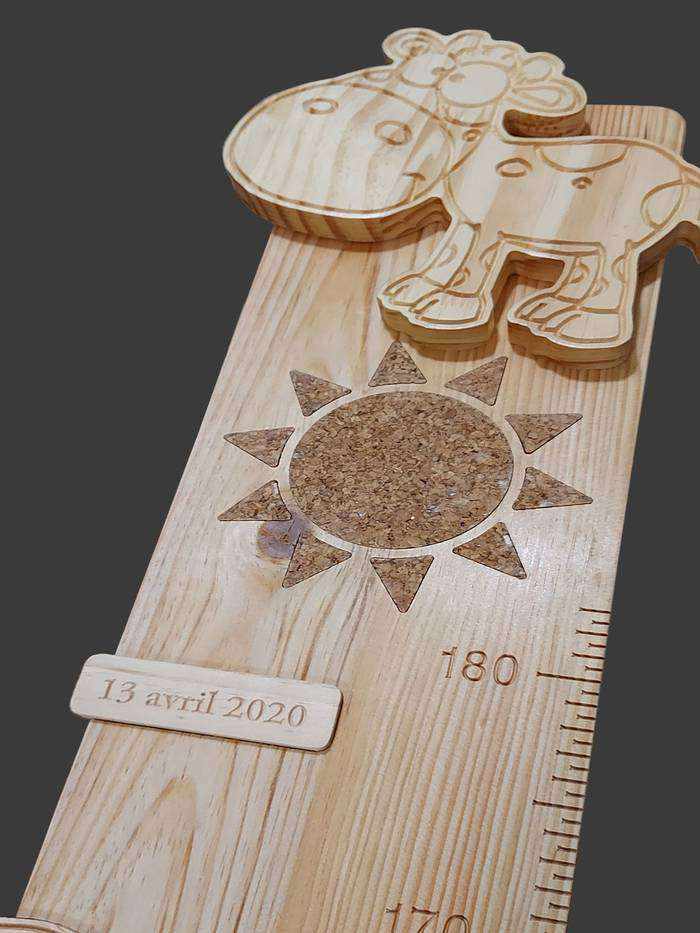 Sur cette toise personnalisée, une jolie vache, la date de naissance  et un soleil incrusté d'un marqueterie de liège.