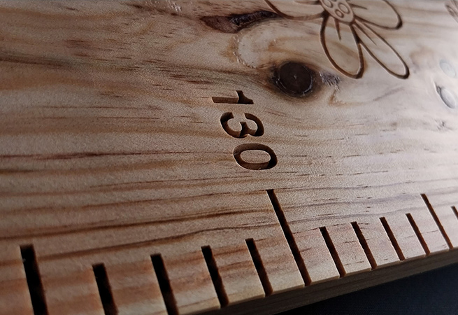 Graduations précises et fleur sculptée sur une toise en bois massif personnalisée, témoignage d’un artisanat unique et raffiné