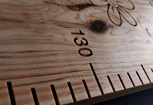 Graduations précises et fleur sculptée sur une toise en bois massif personnalisée, témoignage d’un artisanat unique et raffiné