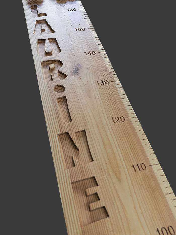 Une grande toise en bois avec pour seuls décors les veines et les nœuds du bois. Prénom et graduations sont mises en valeur.