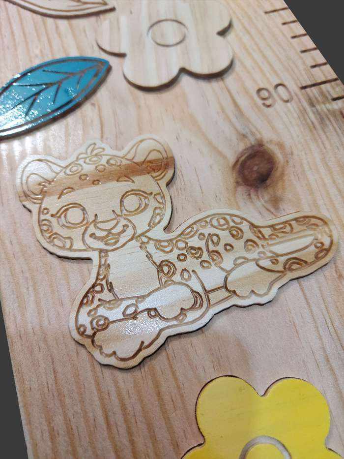 Toise petit léopard en bois, vue de près, avec un léopard souriant parmi des fleurs multicolores et des éléments naturels