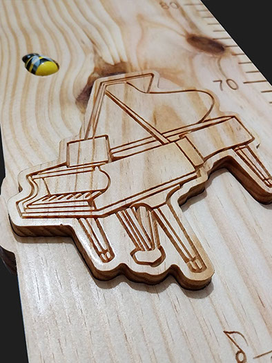 Détail de la toise avec le prénom en écriture cursive incrusté et un nœud naturel bien visible dans le bois.