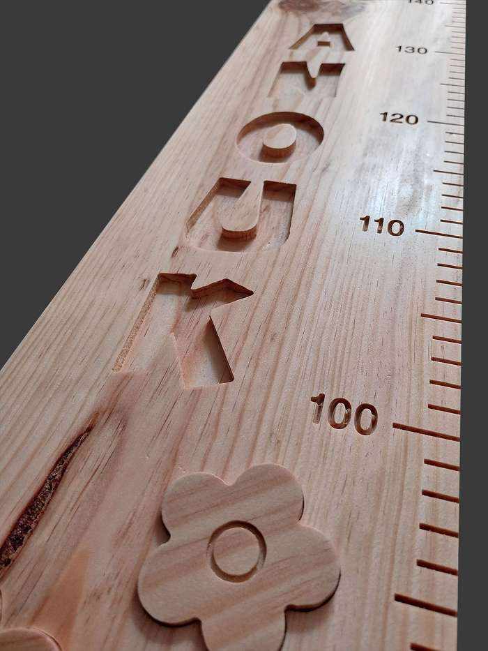 Centre de la toise avec le prénom 'Anouk' sculpté, entouré de petites fleurs de bois, des veines très visibles dans le bois.