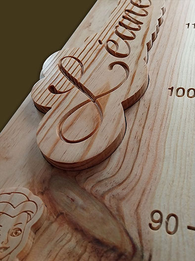 Détail de la toise avec le prénom en écriture cursive incrusté et un nœud naturel bien visible dans le bois.