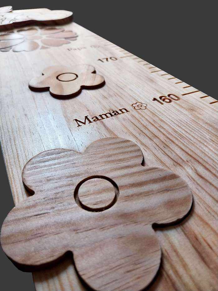 Gros plan d'une toise, des fleurs naturelles, un soleil en liège incrusté et le mot 'maman' sculpté à la hauteur de taille.