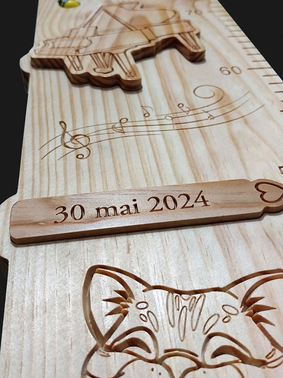 Détail de la toise avec le prénom en écriture cursive incrusté et un nœud naturel bien visible dans le bois.