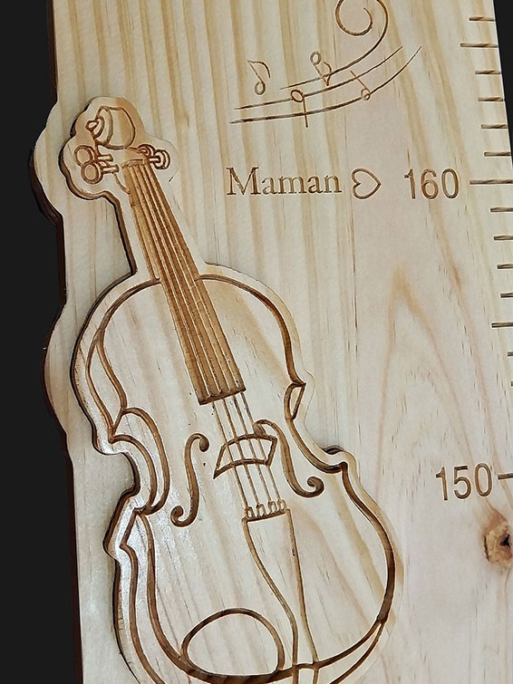 Détail de la toise avec le prénom en écriture cursive incrusté et un nœud naturel bien visible dans le bois.