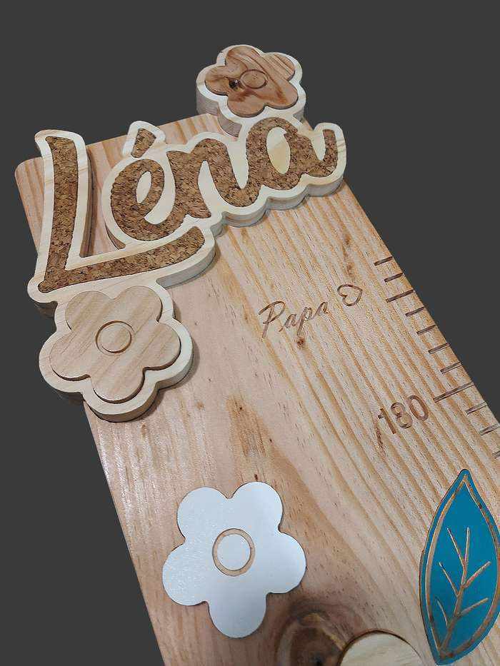 Haut de la toise de Léna, une tête magnifique avec le prénom Léna incrusté en liège dans le bois, accompagné de deux fleurs.